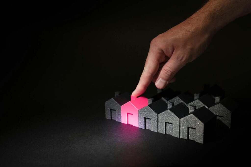A hand selecting a glowing pink house among dark miniature houses, symbolizing real estate choices. How to Choose the Right Business Idea
